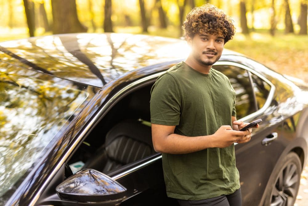 A young man leaning on his car and checking his phone